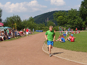 Ein Kind läuft auf der Asche-Rundbahn die 800 m. Im Hintergrund ist weiter weg die Kirkeler Burg zu sehen.